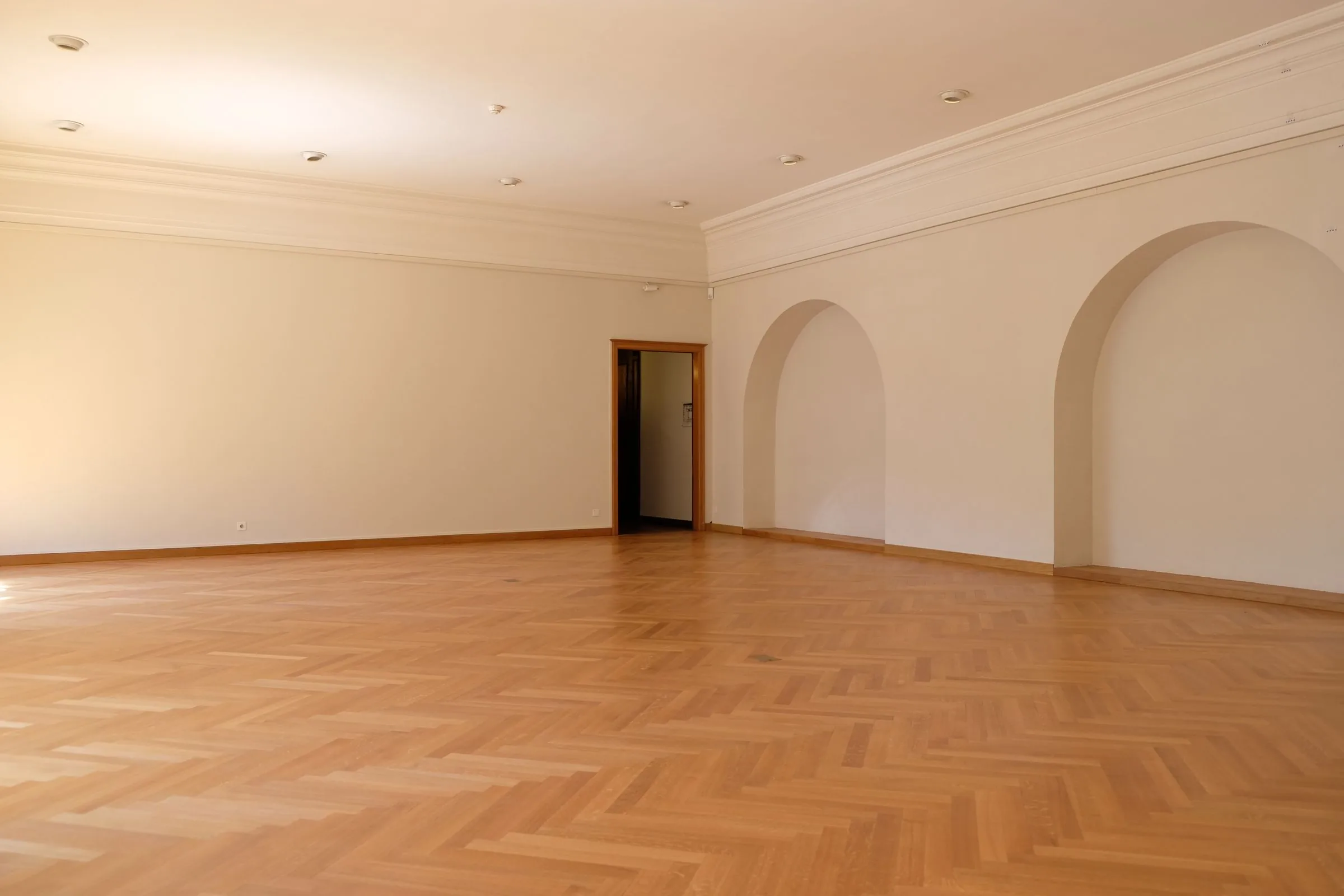 Leerer Altbau-Raum mit hellem Fischgrät-Parkett und Stuckbögen